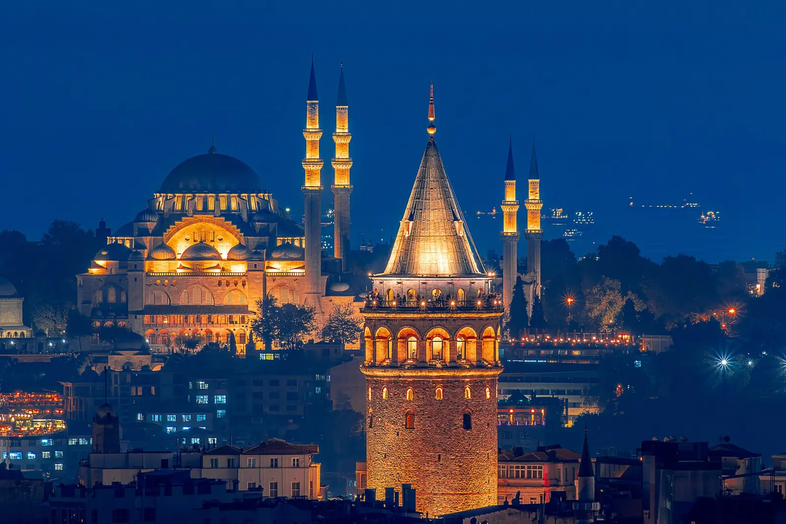 Galata Tower lit up at night with the Süleymaniye Mosque behind
