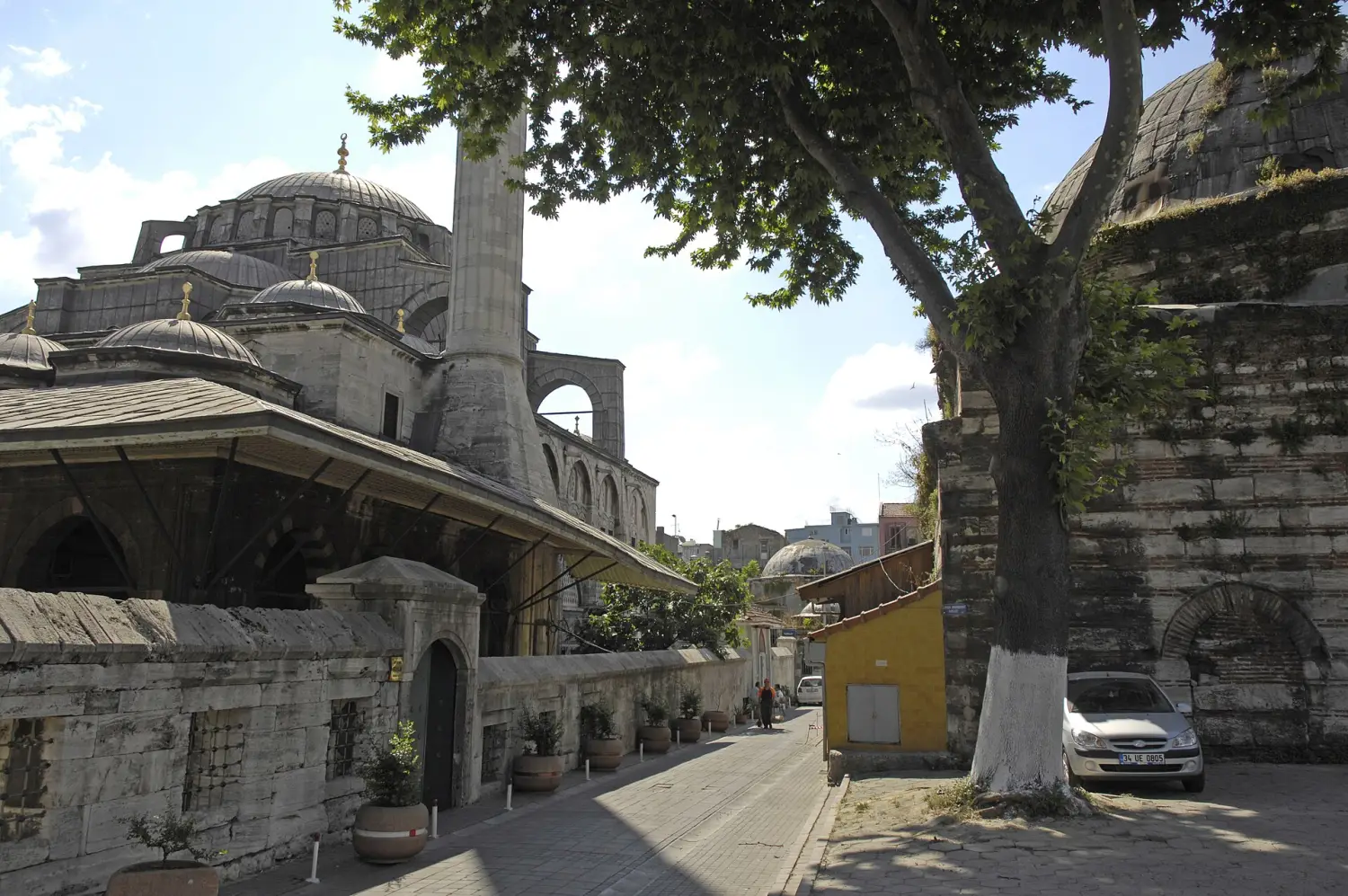The domes and minaret of Kılıç Ali Paşa Mosque from a tree-lined side street